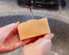 hands holding yellow bar of soap with water running from faucet in background