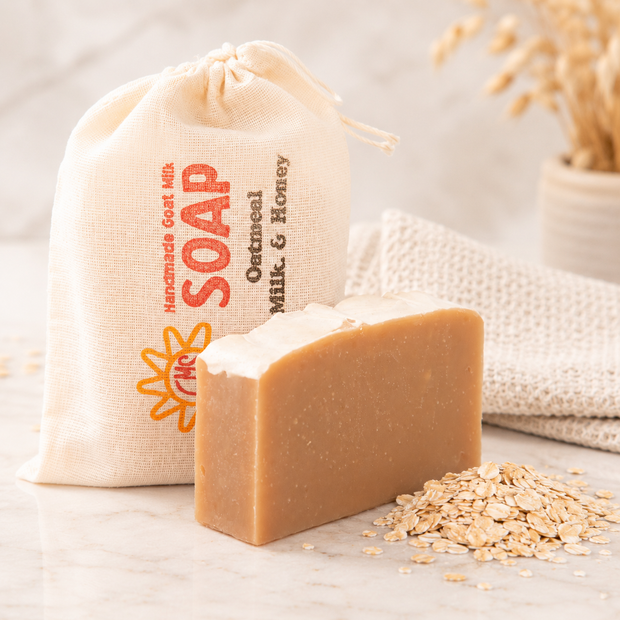 Bar of goat milk soap with oatmeal and a branded drawstring bag on a light background