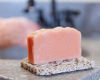 pink bar of soap sitting on soap rest with washing hands in background