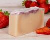 Bar of soap with strawberry scent on a wooden surface.
