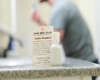 Tooth Powder Trial sitting on countertop with Emery brushing his teeth in the background