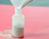 A bag with a cut corner is being used to fill a tooth powder bottle with Tooth Powder