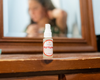 Jade looking in mirror with small perfume spray bottle sitting on dresser