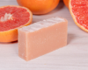 Bar of soap with grapefruit scent on a wooden surface with grapefruits.