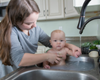 Woman and baby washing hands in a kitchen sink.