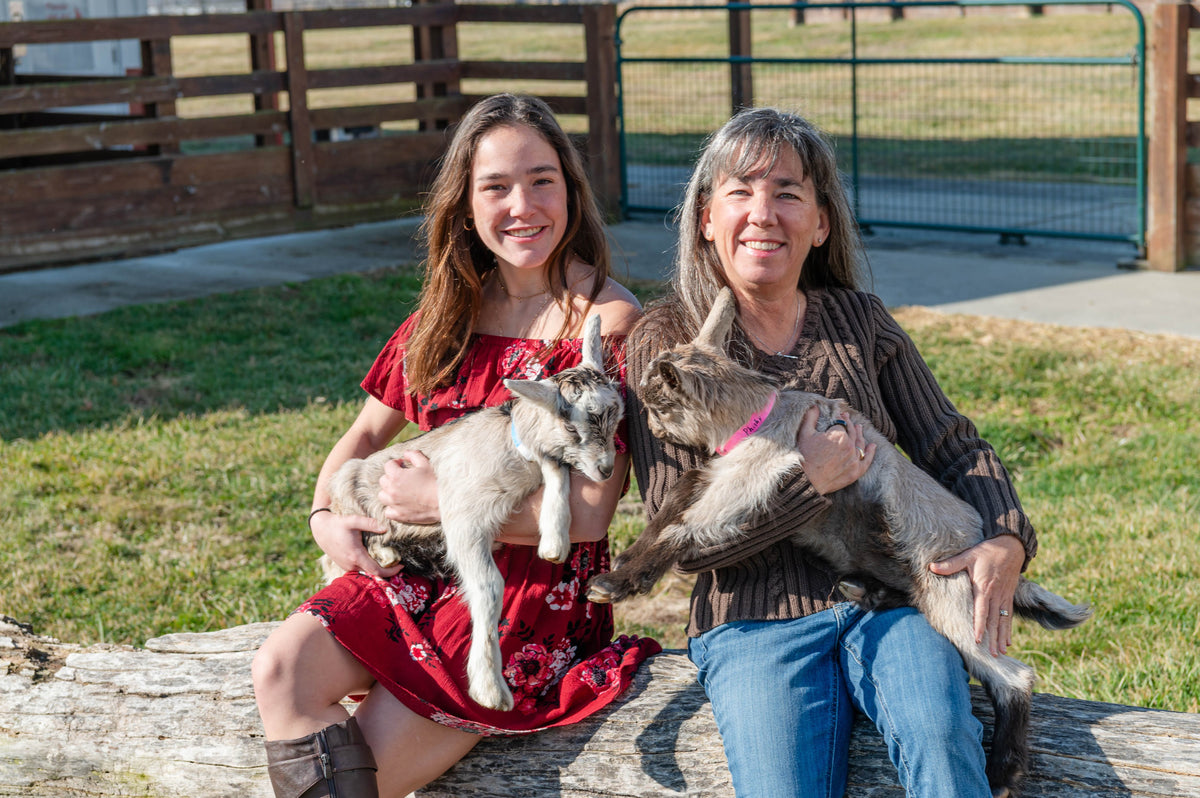 Three generations of the Goat Milk Stuff family holding baby goats on the farm