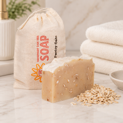 Bar of goat milk soap with oatmeal on a marble surface next to a drawstring bag labeled 'Soap' and folded towels.