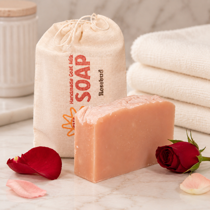 Bar of goat milk soap with a drawstring bag labeled 'Soap' and a rosebud on a marble surface.