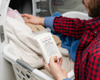 Holding a pack of Goat Milk Laundry Soap while loading clothes into the washing machine