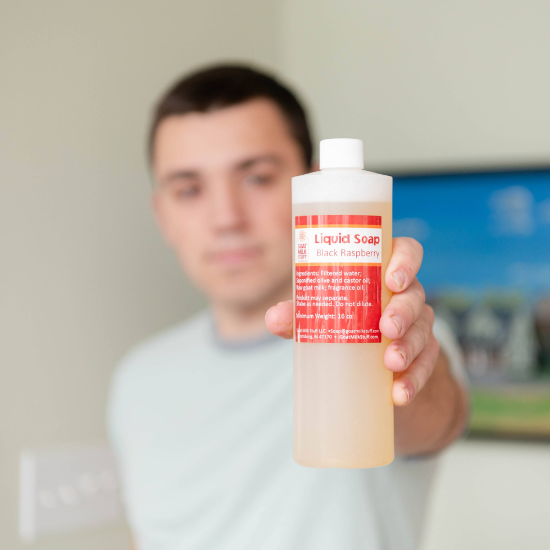 Person holding a bottle of black raspberry goat milk stuff liquid soap with a red label in front of a blurred background