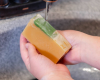 hands holding yellow bar of goat milk soap with green swirl above sink