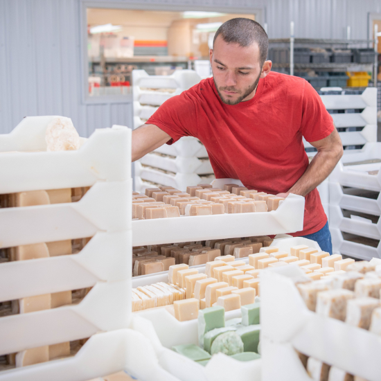 Colter organizing Goat Milk Soap bars on shelves in a soap production area