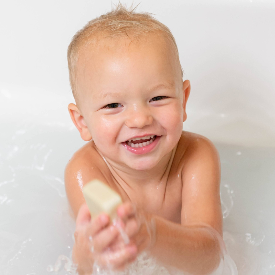 Baby taking a bath while holding a goat milk bar soap