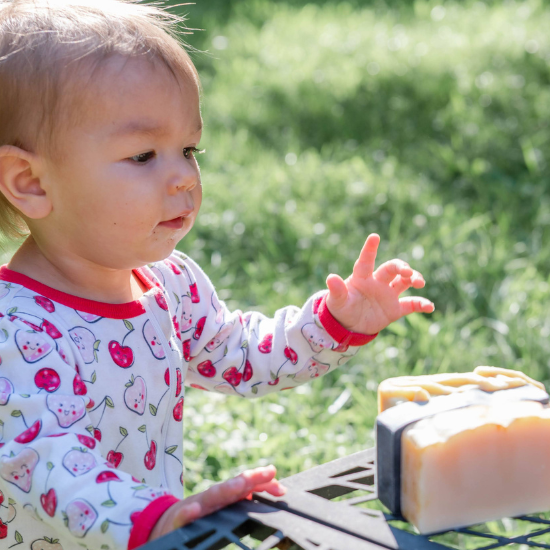 Baby reaching toward a stack of Goat Milk Soap bars on an outdoor table