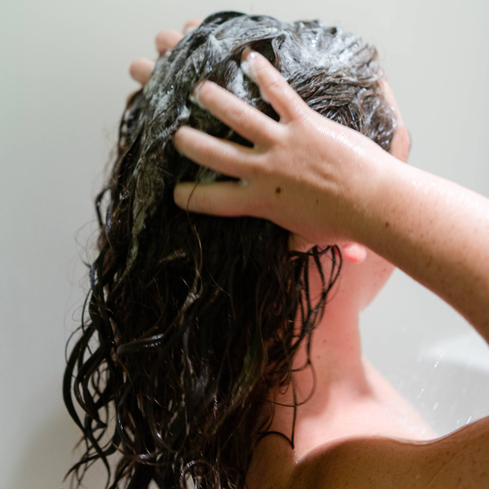 Woman bathing while brushing her lathered hair with her fingers using Goat Milk Soap