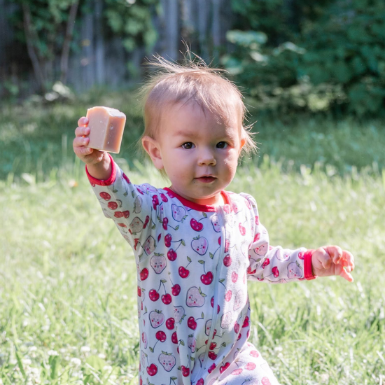 Baby holding a Goat Milk Soap bar in an outdoor setting