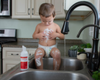 Baby sitting by a sink with goat milk liquid soap beside him