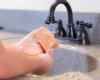 Person washing hands under a faucet in a sink.