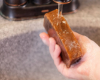 hand holding brown goat milk soap under running water from faucet